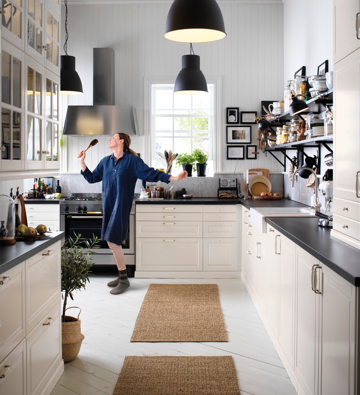 Helle Küche im modernen Landhausstil mit weißen Fronten und schwarzen Arbeitsplatten. Zwei rechteckige Küchenläufer aus Naturmaterial liegen vor der Arbeitsfläche und sorgen für Komfort beim Kochen.