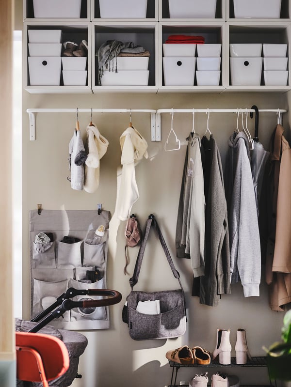 A MULIG clothes bar on a hallway wall holding outdoor clothes, with a LEN hanging storage and hooks on the wall below it.