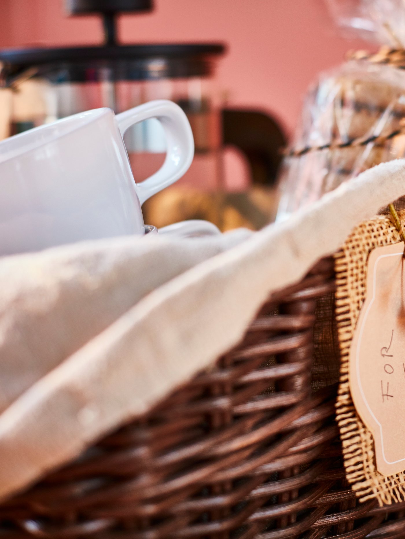 En närbild på en kaffekorg som innehåller en vit mugg, kakor och en kaffepress i en flätad korg.