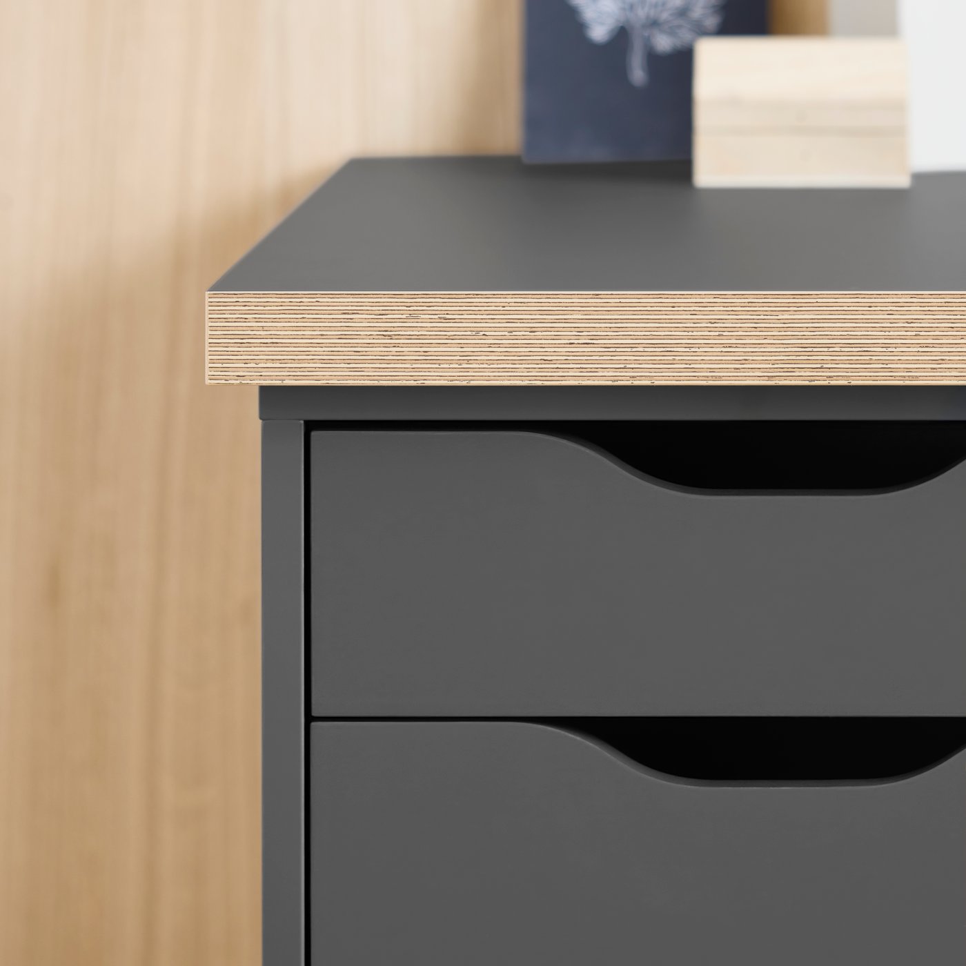 A close-up of a dark grey ALEX drawer unit beneath a dark grey/wood-effect LAGKAPTEN tabletop.