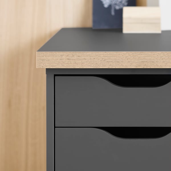 A close-up of a dark grey ALEX drawer unit beneath a dark grey/wood-effect LAGKAPTEN tabletop.