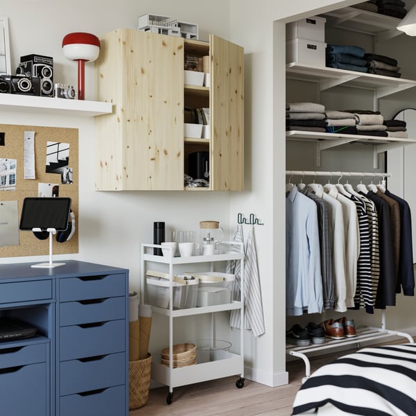 An IVAR cabinet in pine attached to the wall with a white NISSAFORS trolley underneath filled with steel mesh baskets.