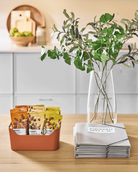 Es sind drei unterschiedliche MUNSBIT Nusspackungen in einer Box auf einem Tisch, neben einer Vase und Unterlagen.