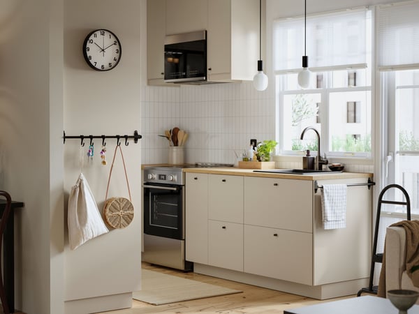 A small, bright kitchen with white walls has beige HAVSTORP fronts and two SUNNEBY cord sets in black textile in the window.