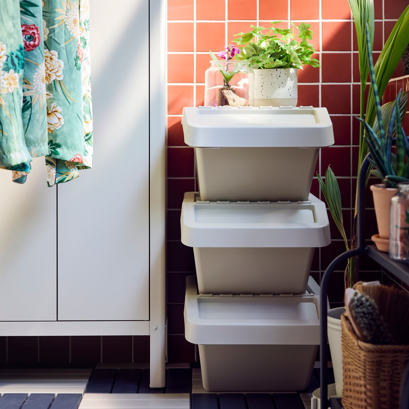 A balcony with three beige SORTERA sorting bins with lid stacked on top of each other against a pink tiled wall.