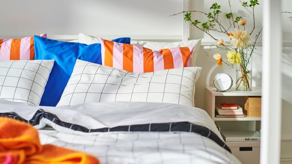 Close-up of bed with a lot of pillows in different patterns and colours. Bedside table on the right.