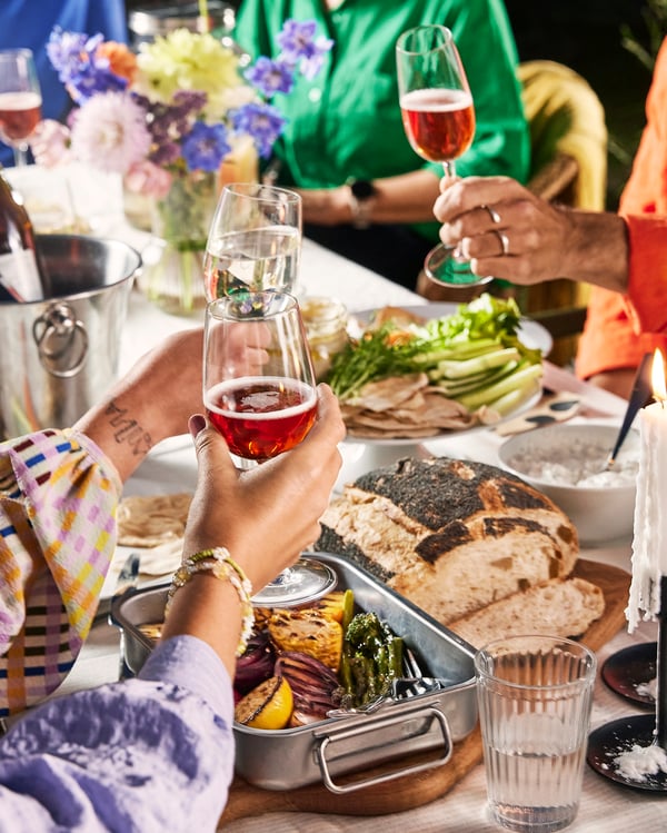 An image of a full dining table where a person holds out a glass and toasts.