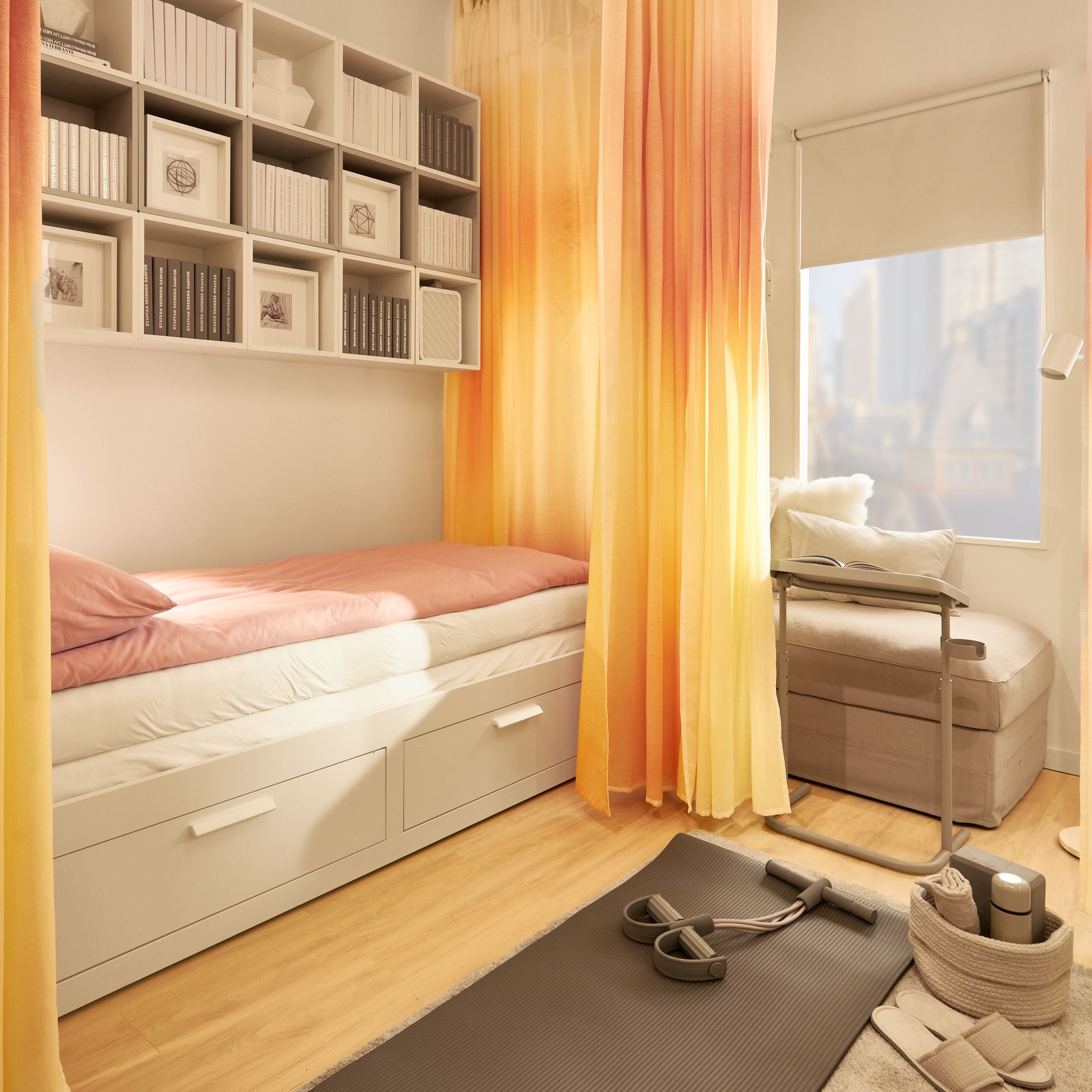 O canapea extensibilă albă cu două sertare lângă perete. Deasupra canapelei sunt unități de depozitare cubice pline cu cărți și cutii. În jurul canapelei sunt perdele vopsite în galben și roz.