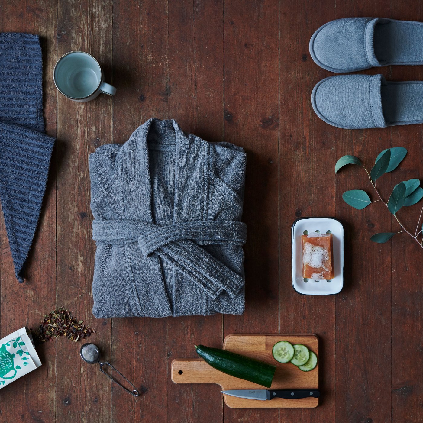 Ein Badmantel, Haarhandtuch, Pantoffel und Teetasse die auf einem Holzboden liegen