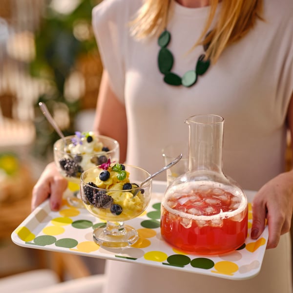 BRÖGGAN tray with BRÖGGAN carafe and class on top being carried by a woman in a white top.