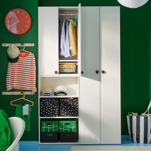 A LASTARE wardrobe combination in white with open shelves and storage boxes, against a wall in a green children’s bedroom.