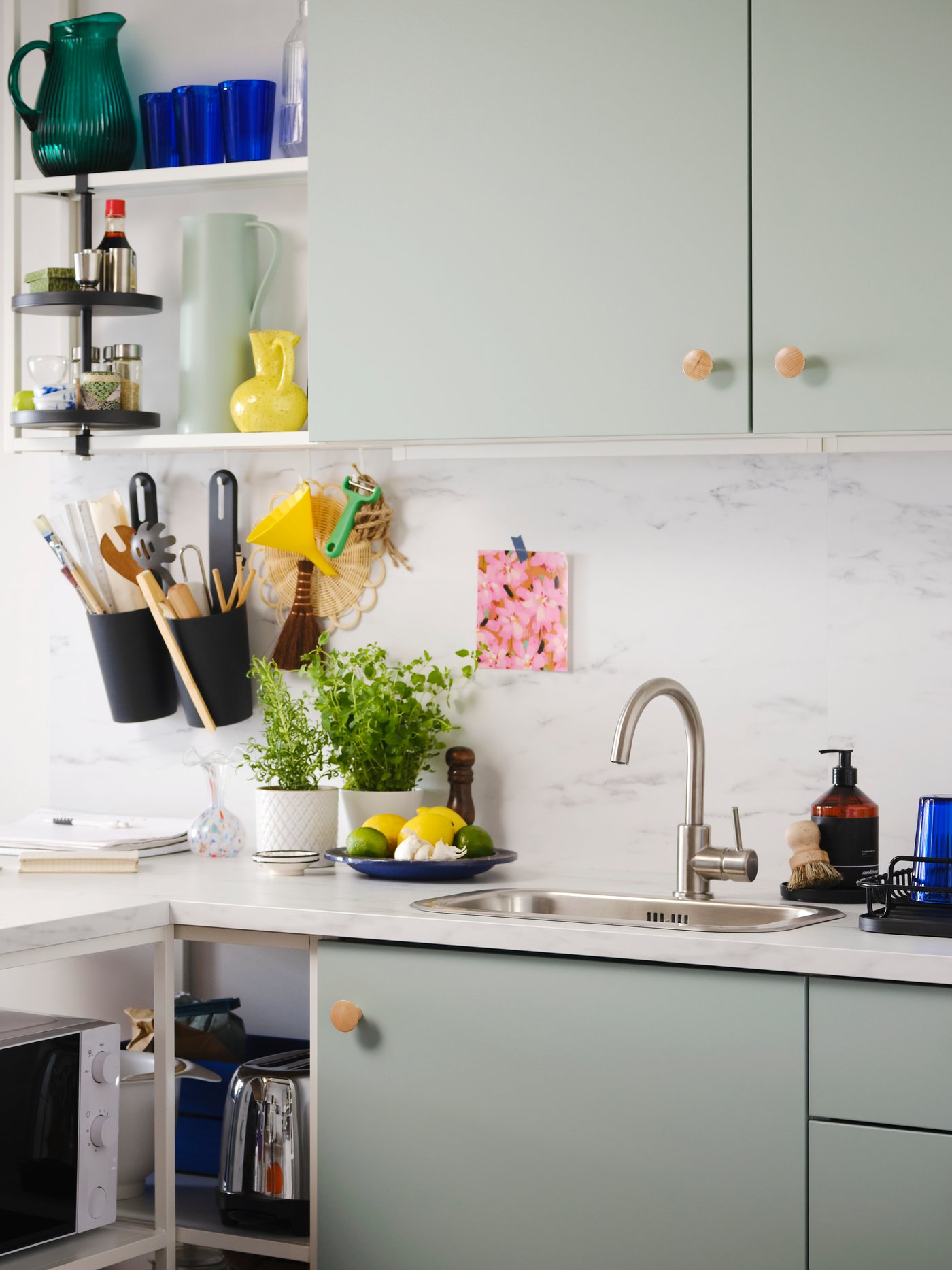 Eine Küche mit ENHET Fronten in blassem Graugrün, einem ENHET Regalrahmen in Weiß und einem ENHET Drehregal.