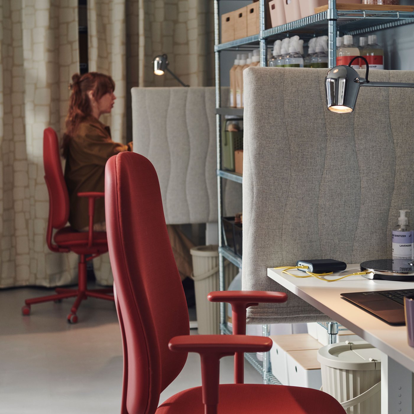Two workstations with MITTZON acoustic screens for desks and red SMÖRKULL office chairs are separated by metal shelves.