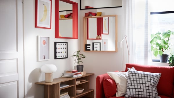 A TURBOKASTANJ mirror, a red TURBOKASTANJ mirror and some works of art hang on the walls in a corner of a living room.