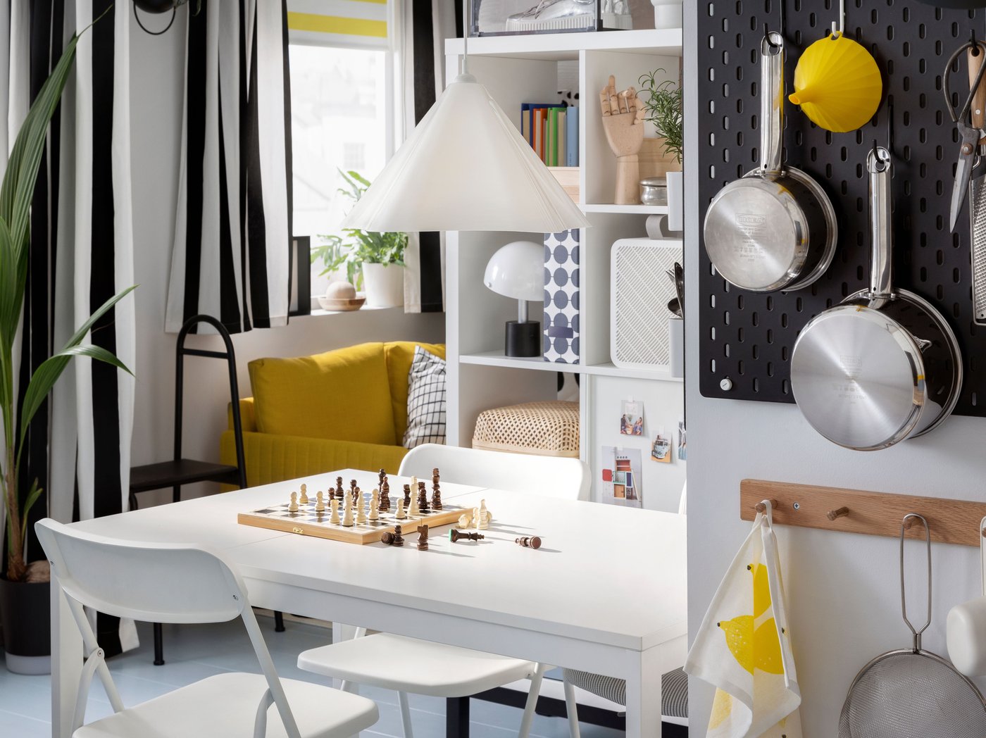 A VIHALS extendable table and VIHALS folding chairs stand in a small dining room area under a white ZEBRASÄV pendant lamp.