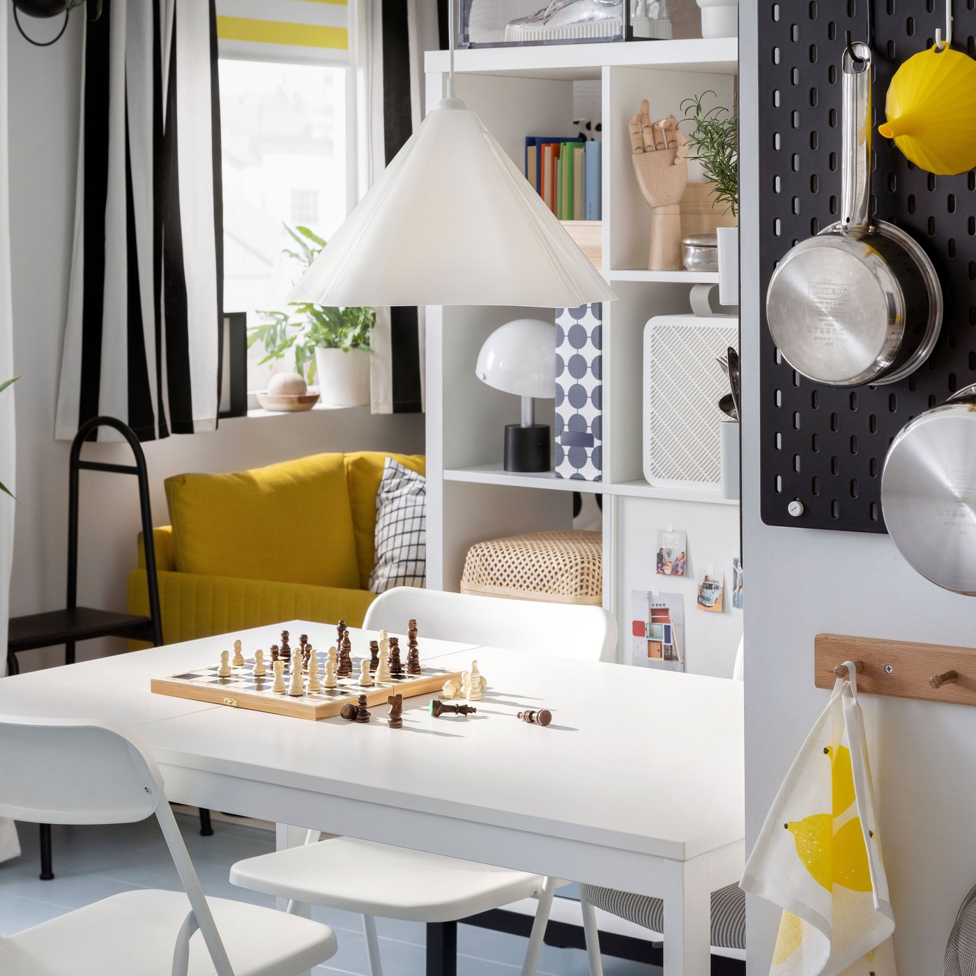 Rozkładany stół VIHALS i składane krzesła VIHALS ustawione w niedużej jadalni pod białą lampą wiszącą ZEBRASÄV.