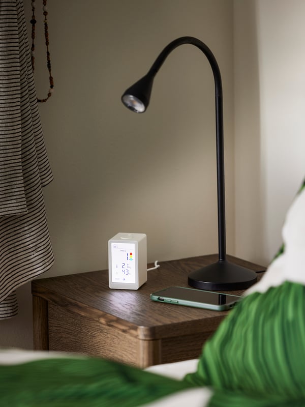 A black NÄVLINGE LED clamp spotlight attached to a bookshelf and with light directed down on to a desk.