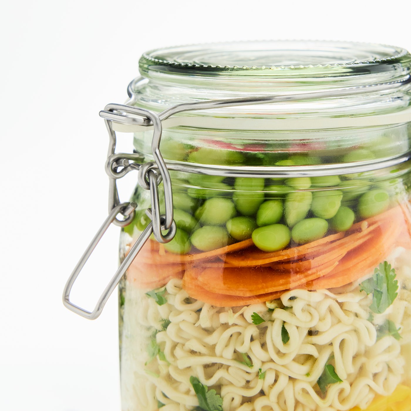 Es ist eine Nahaufnahme einer KORKEN Dose aus Glas mit luftdicht schliessendem Deckel zu sehen. Darin befinden sich verschiedene Schichten Lebensmittel.