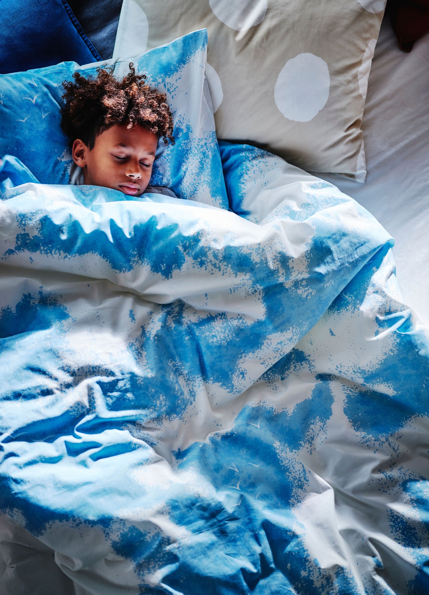 Ein Junge kuschelt sich in blau weiße ÄNGSVITVINGE Bettwäsche und schläft.