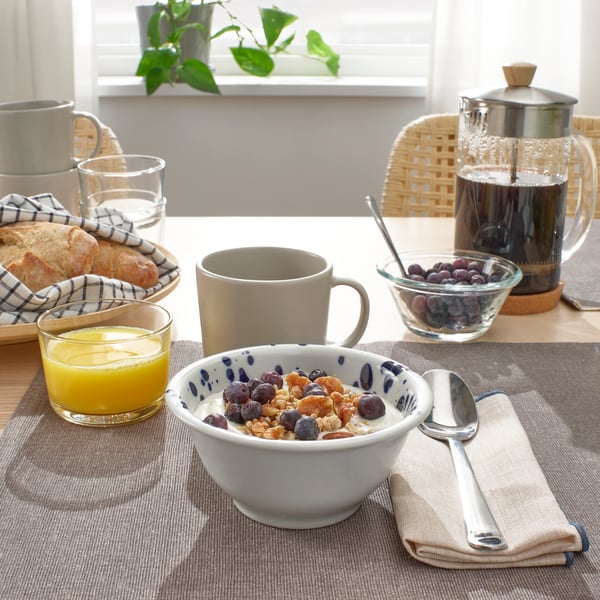 Eine SILVERSIDA Schüssel mit Müsli gefüllt steht auf einem gedeckten Frühstückstisch zusammen mit Orangensaft, einer Tassse und einem Kaffeezubereiter.