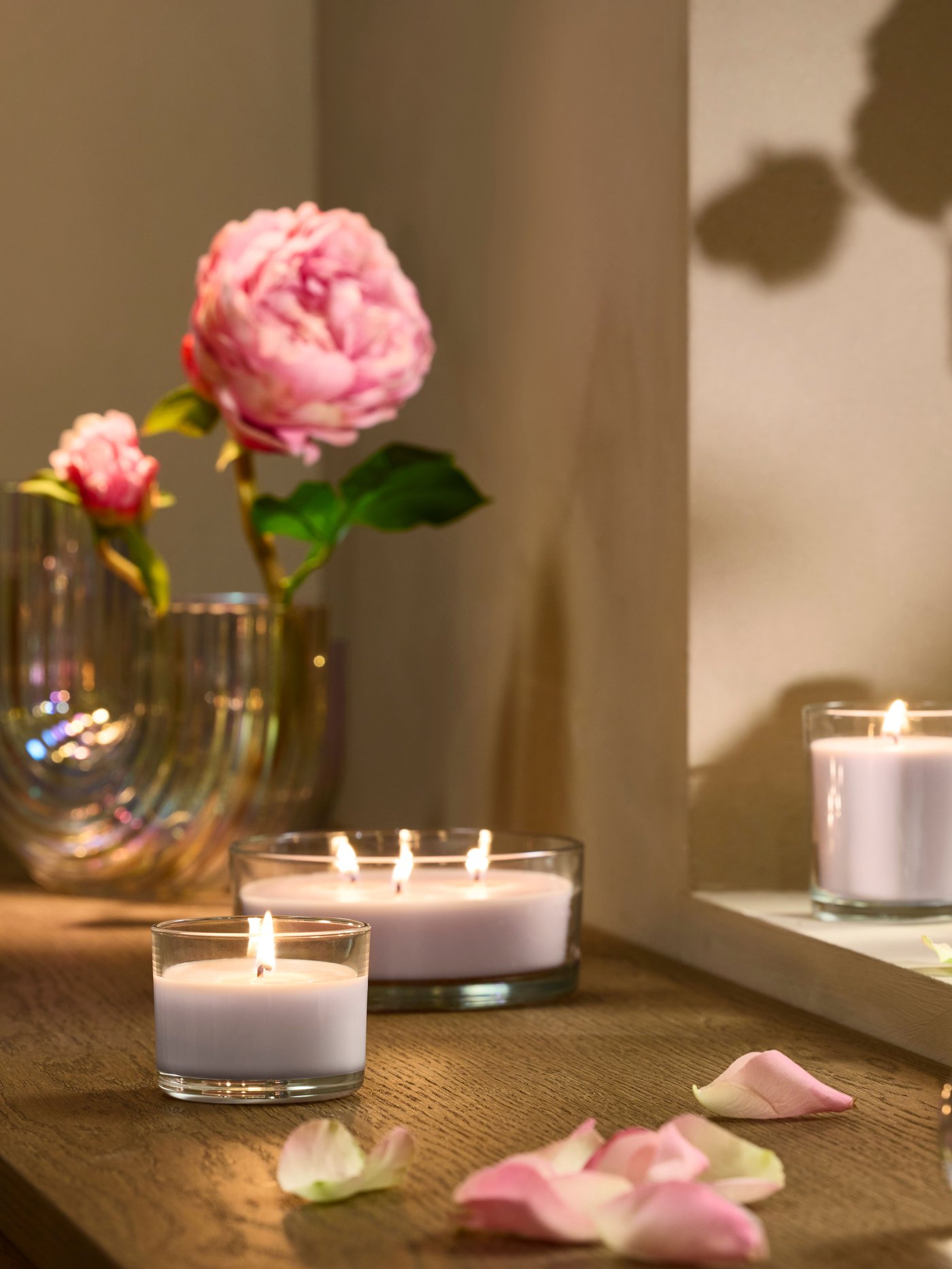 Ett ljusrosa LOTSFÅGEL doftljus i glas med rosa blommor