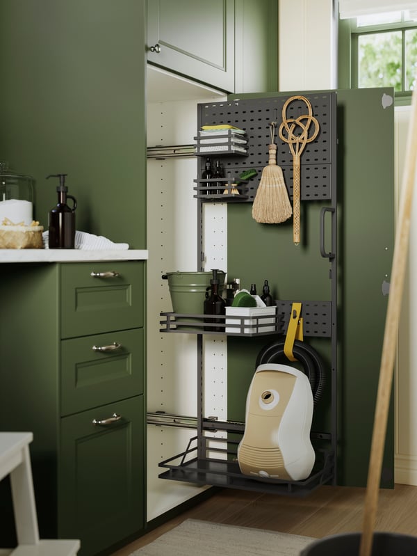 Accessori interni per i prodotti per le pulizie UTRUSTA perfettamente organizzati con scopa, articoli per la pulizia e un aspirapolvere, all'interno di un elemento contenitore in una cucina verde.