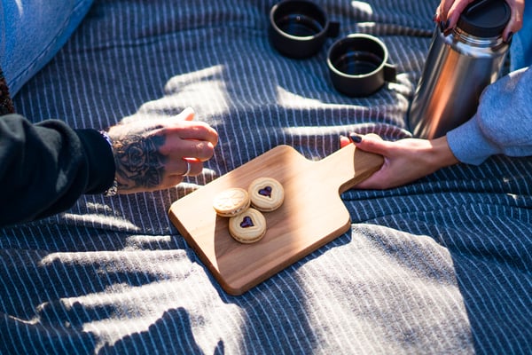 A small cutting board filled with heart-shaped biscuits, two mugs of hot coffee and thermo filled with coffee.