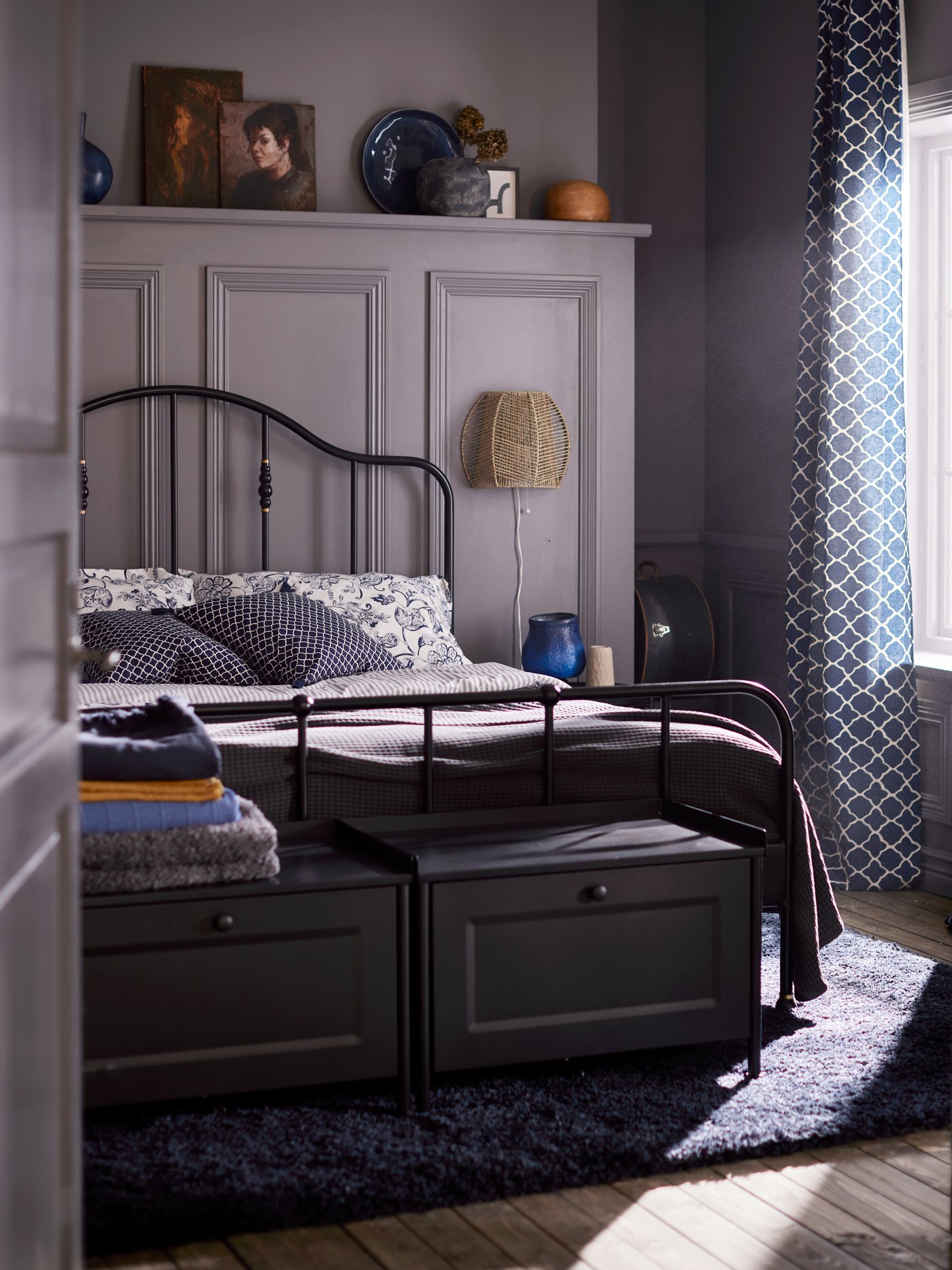 Two black storage benches and a bed with a black SAGSTUA bed frame made with blue floral bed linen on a dark blue rug.