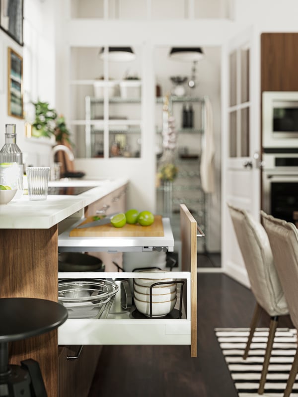 A kitchen with an open UTRUSTA pull-out work surface in focus and a pantry and some appliances in the background.