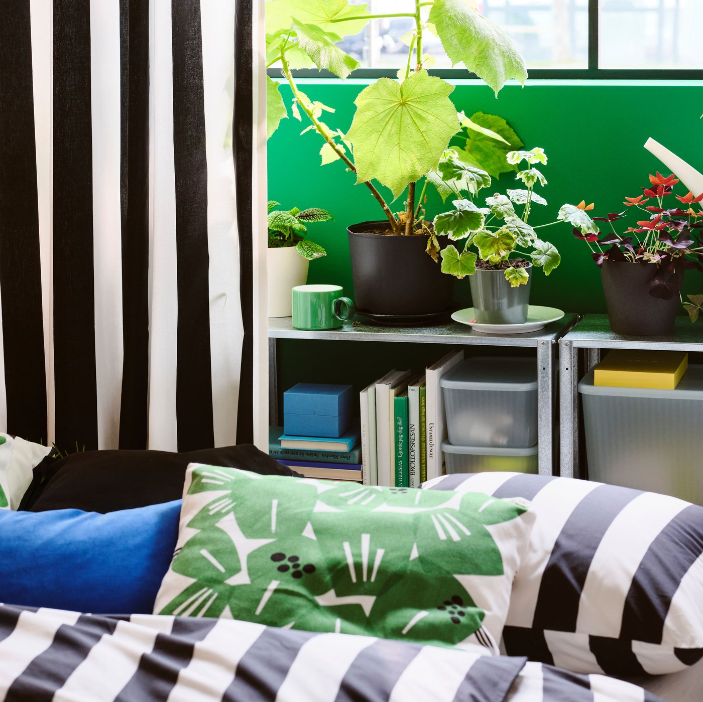 Plants in pots on a HYLLIS shelving unit in front of a window framed by a curtain made from VARGTÖREL pre-cut fabric.