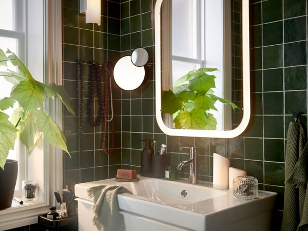A bathroom with a white mirror with integrated lighting over a wash-stand, plus light green guest towels and a potted plant.