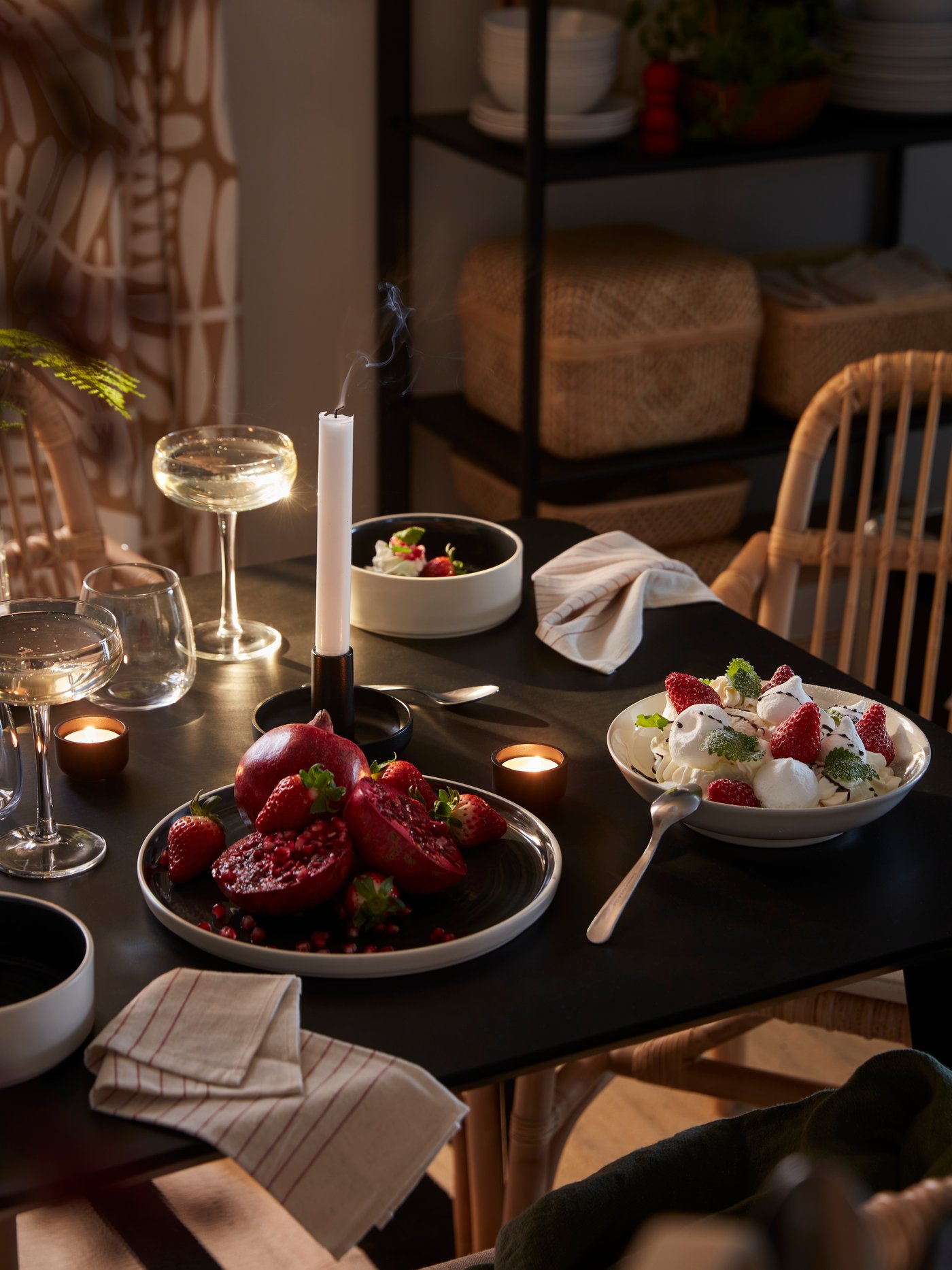 A LISABO table set with a candlelit meal, with dessert, drink in DYRGRIP coupe glasses and pomegranate on an OMBONAD plate.