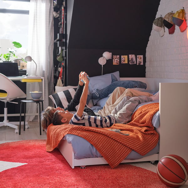 Two teen age boys lie on their backs looking at a handheld game console on a VIHALS bedframe with an extended trundle bed.