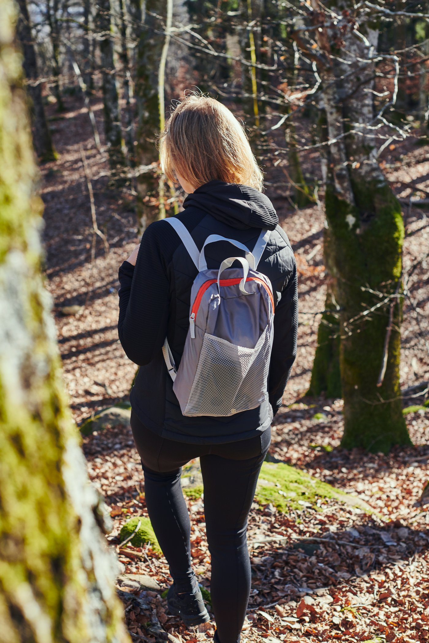 En pige går i en skov med en PIVRING rygsæk på ryggen.