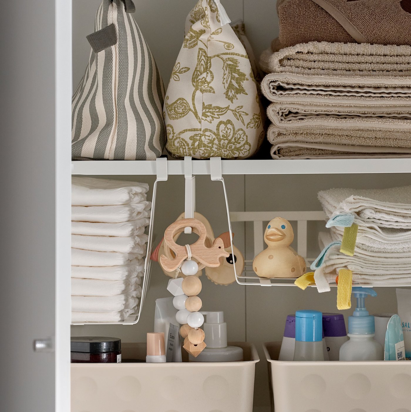 NOJIG organisers on a cabinet shelf holding fabric bags, folded towels and cleaning products alongside other stored items.