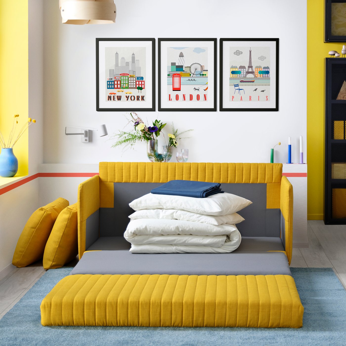 Un sofá cama FRIDHULT amarillo abierto con almohadas y ropa de cama listos para armar una cama.