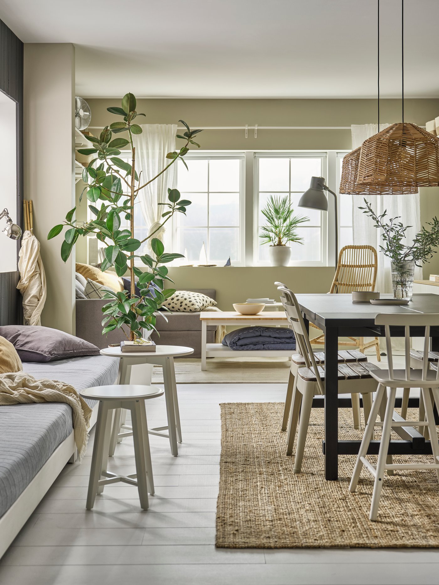 A light open dining and living room in neutral tones, grey sofas, dark brown dining table, white chairs and large plants.