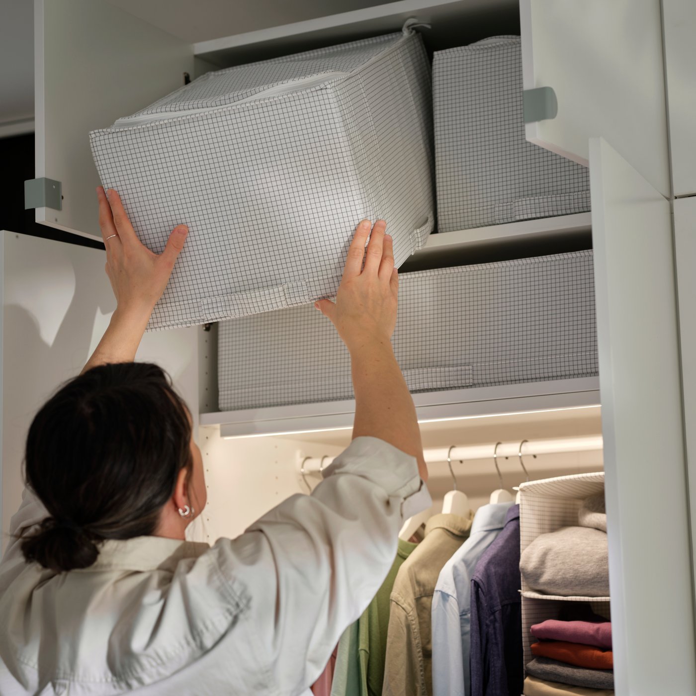 STUK storage case in white pattern being placed on the top shelf of a wardrobe with hanging clothes below.