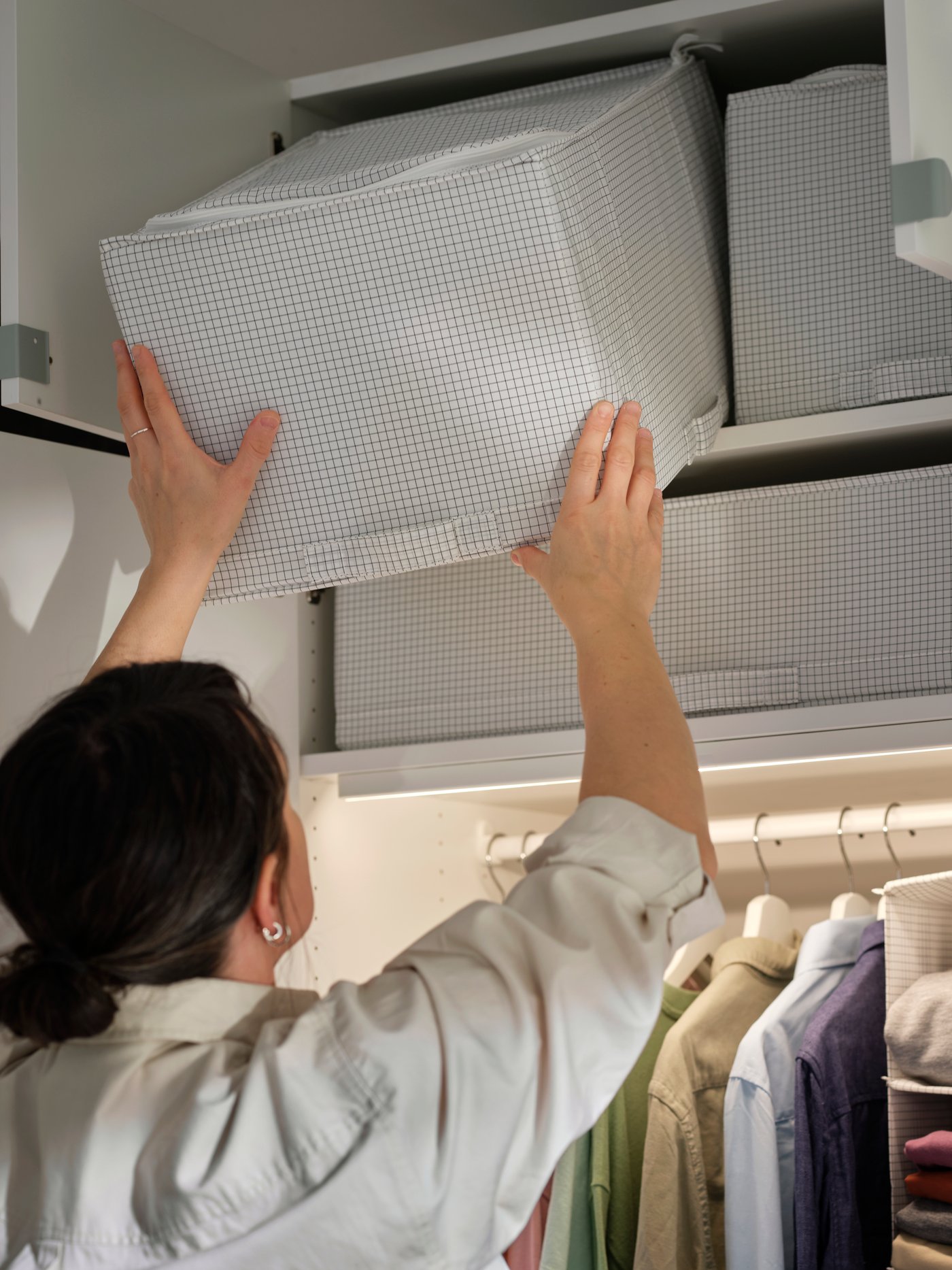 Una custodia STUK a fantasia bianca viene posizionata sul ripiano superiore di un armadio con vestiti appesi sotto.