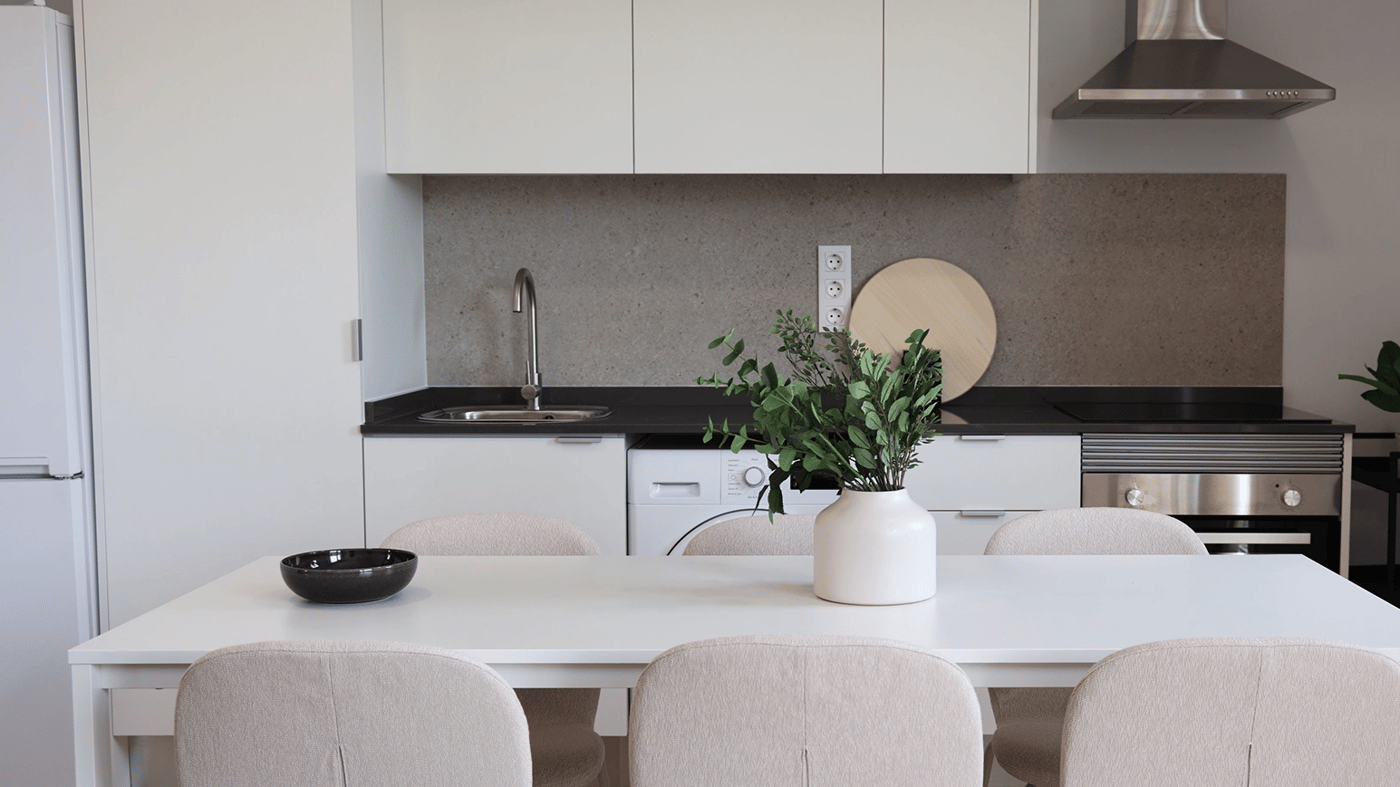 White dining table with six beige chairs, and a linear kitchen behind it