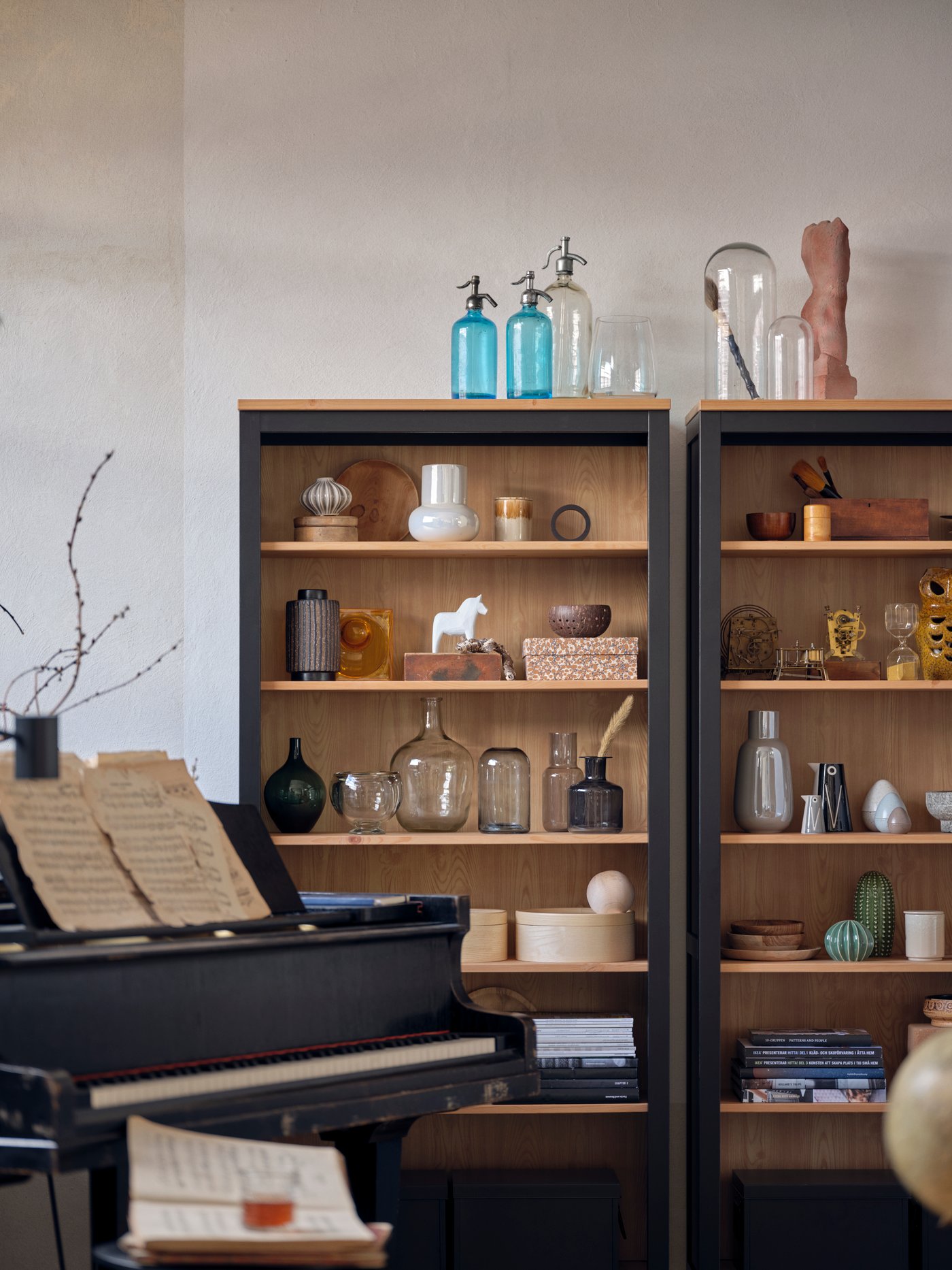 Dos librerías con jarrones grises y blancos, cajas con tapa y otros artículos. Hay un piano junto a una de ellas.