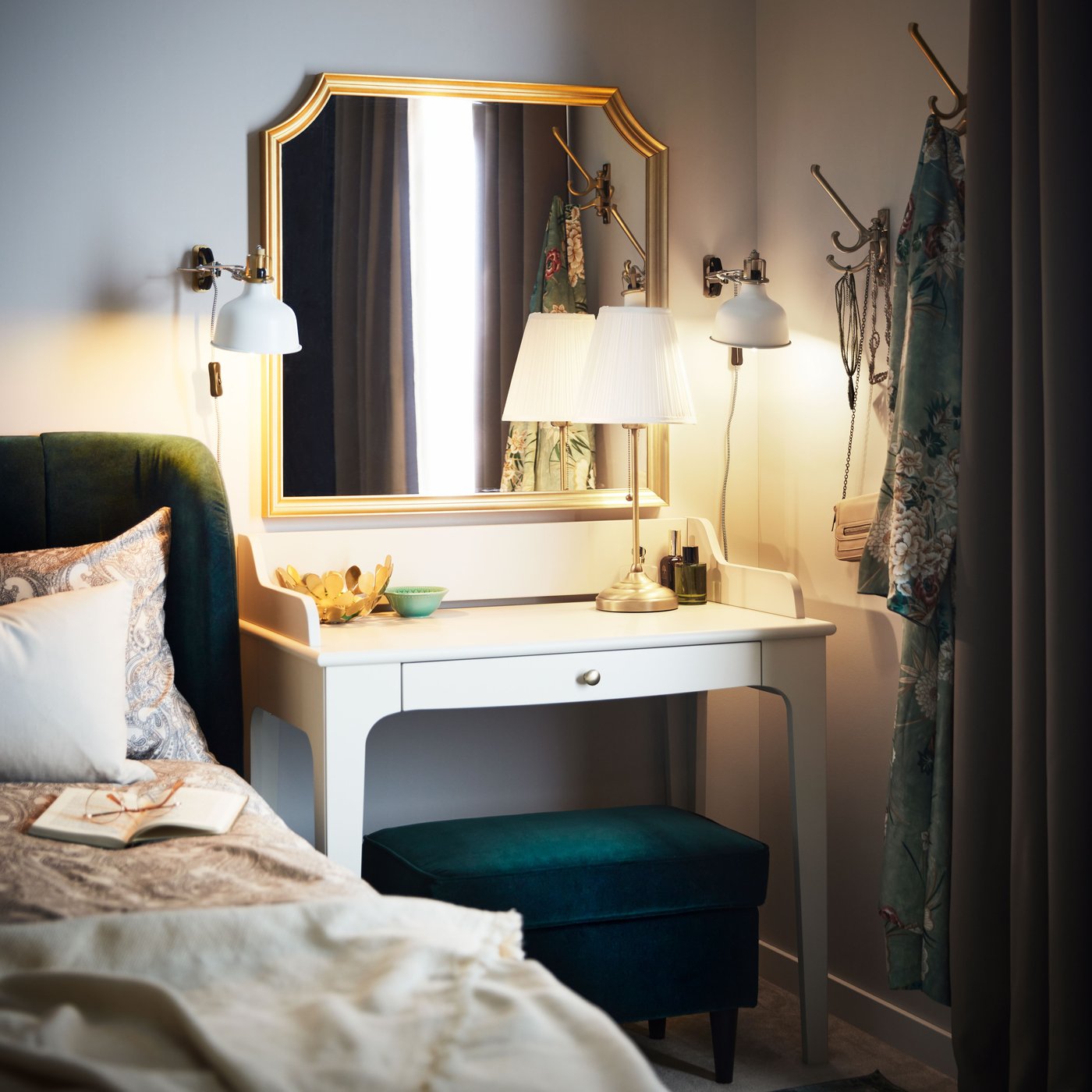 Ett ljusbeige LOMMARP skrivbord står i ett hörn under en SVANSELE spegel bredvid en mörkgrön TUFJORD-klädd säng.
