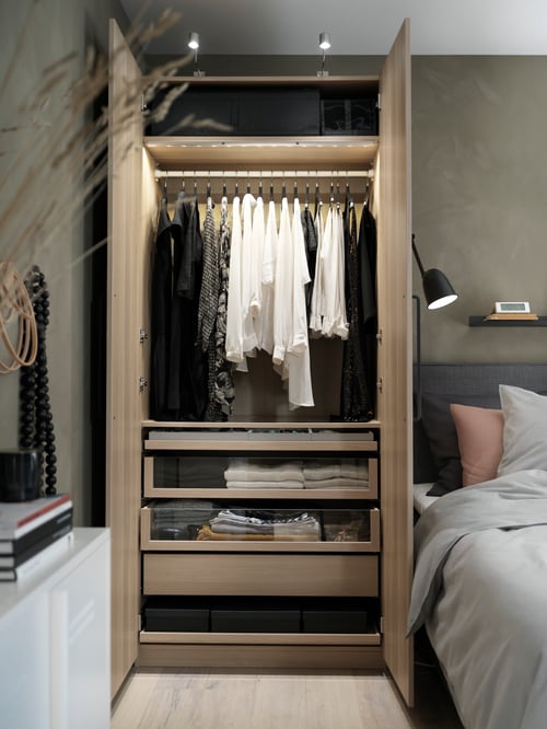 Bedroom with dark olive-green walls, wardrobe with clothing and LED cabinet lighting, bed frame with pillows and work lamp.