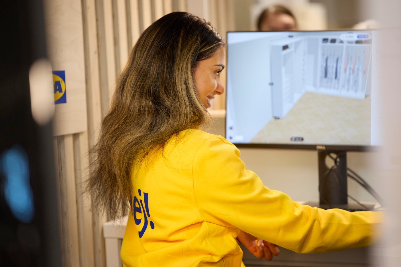 Person in a yellow IKEA uniform using a computer to plan a storage solution on a screen.