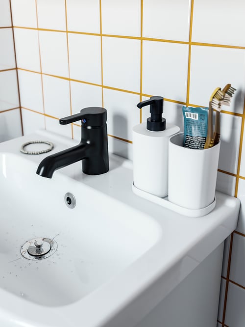 A three piece bathroom set consisting of a soap dispenser, a toothbrush holder, and a tray, all set on a white wash-basin. 