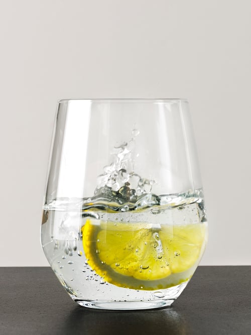 Gros plan d’un verre d’eau et d’une tranche de citron. L’eau est poussée vers le haut par l’élan de la tranche. 