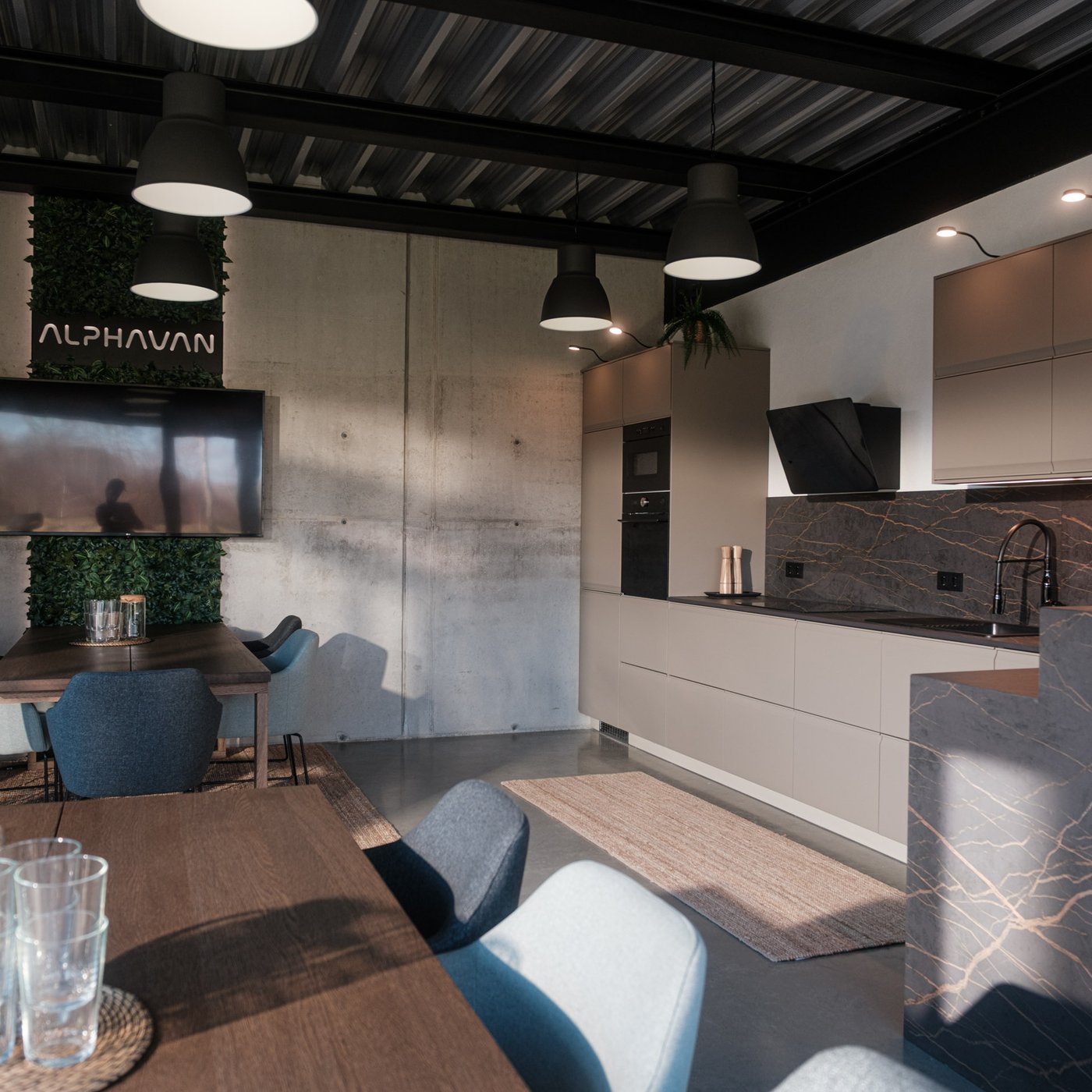 Moderne Küche mit beigen Schränken, schwarzer Dunstabzugshaube, Esstisch, Hängelampen, und Barbereich mit Hockern und Pflanzen