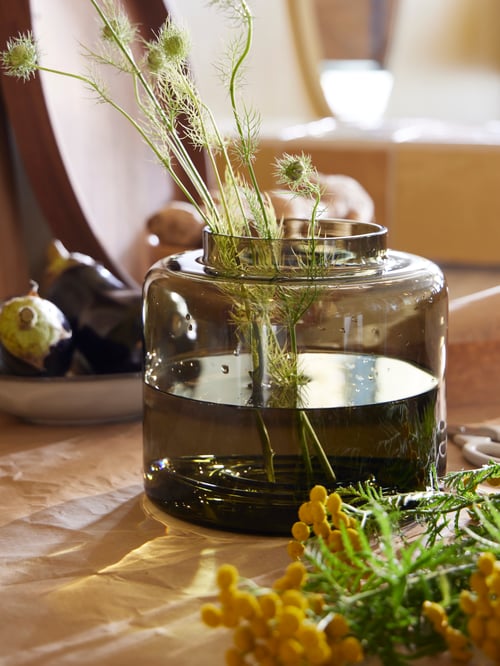 Close-up of a green-brown KONSTFULL vase, next to a tray and  a bowl, in a modern living room setting. 