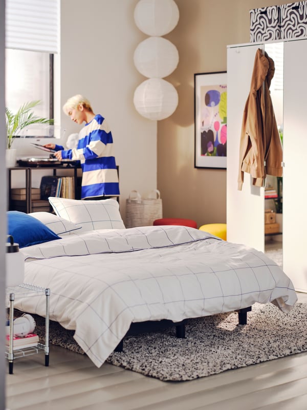 Male student in brown and white college bedroom with sofa-bed made with white and blue check bedding in centre.