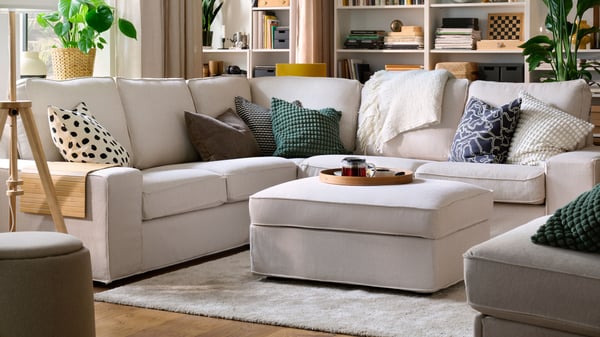 Ein hellbeiges KIVIK Ecksofa mit TRESUND Bezug als 4-Sitzer Ecksofa im Wohnzimmer. Davor ein KIVIK Hocker als Couchtisch. 